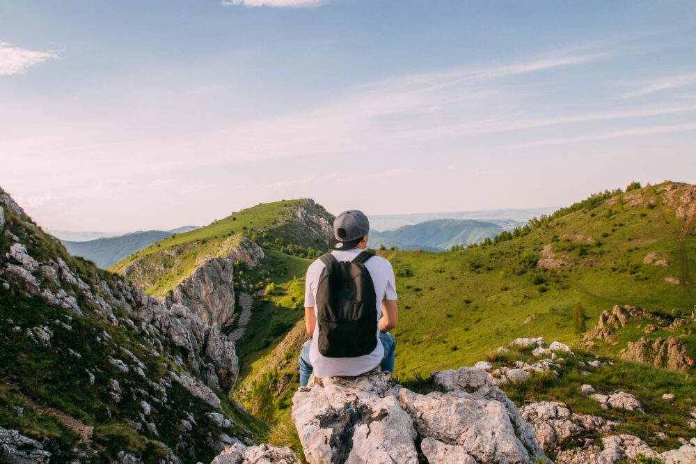 man sitting on rock facing the grass covered mountains